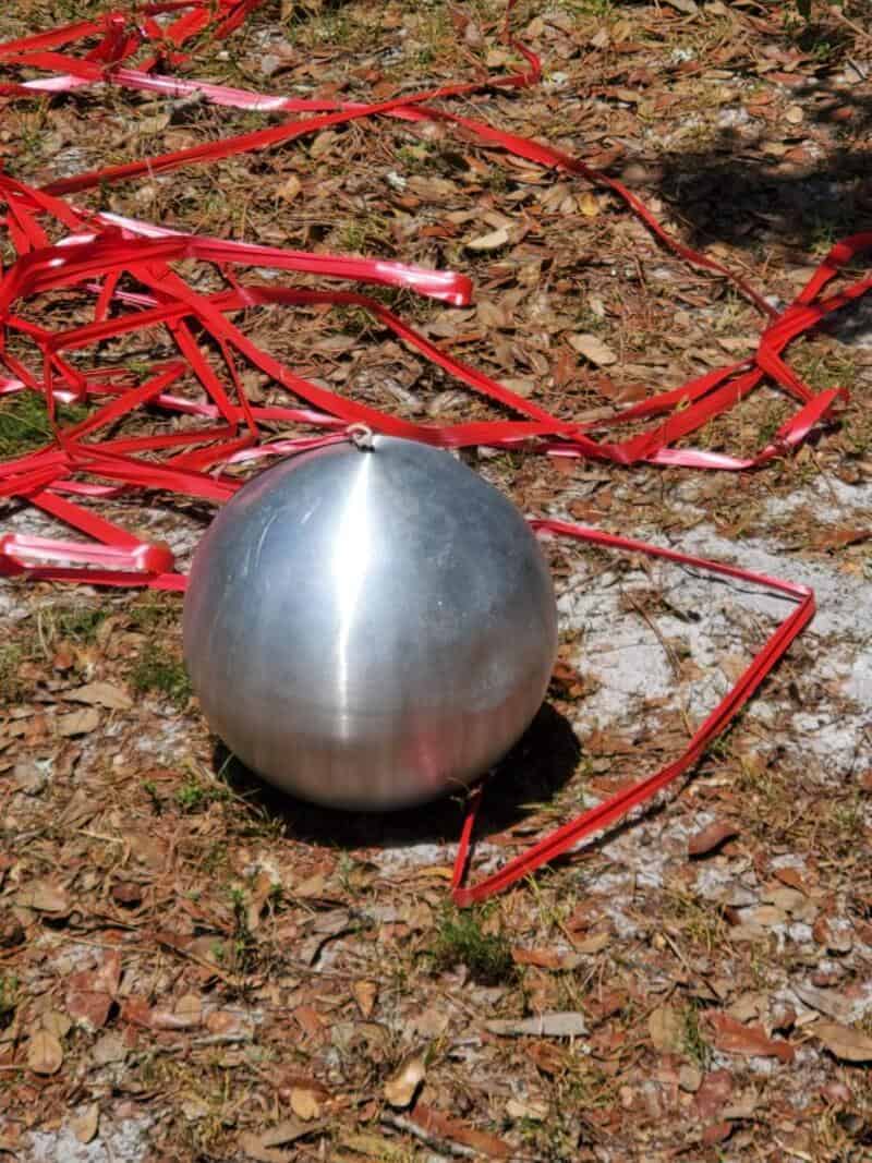 Metal sphere on ground with red ribbons around it, outdoors.