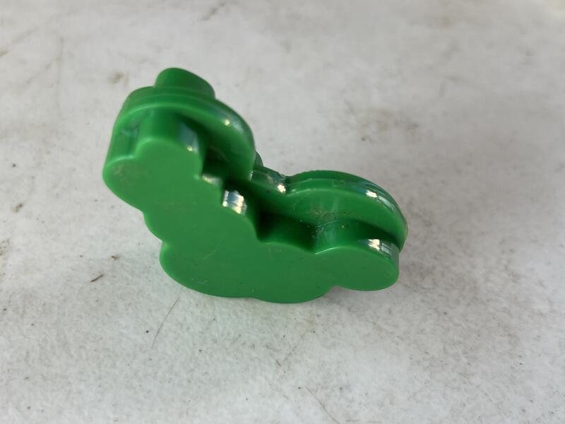 Green plastic toy in the shape of a dinosaur on a gray surface.