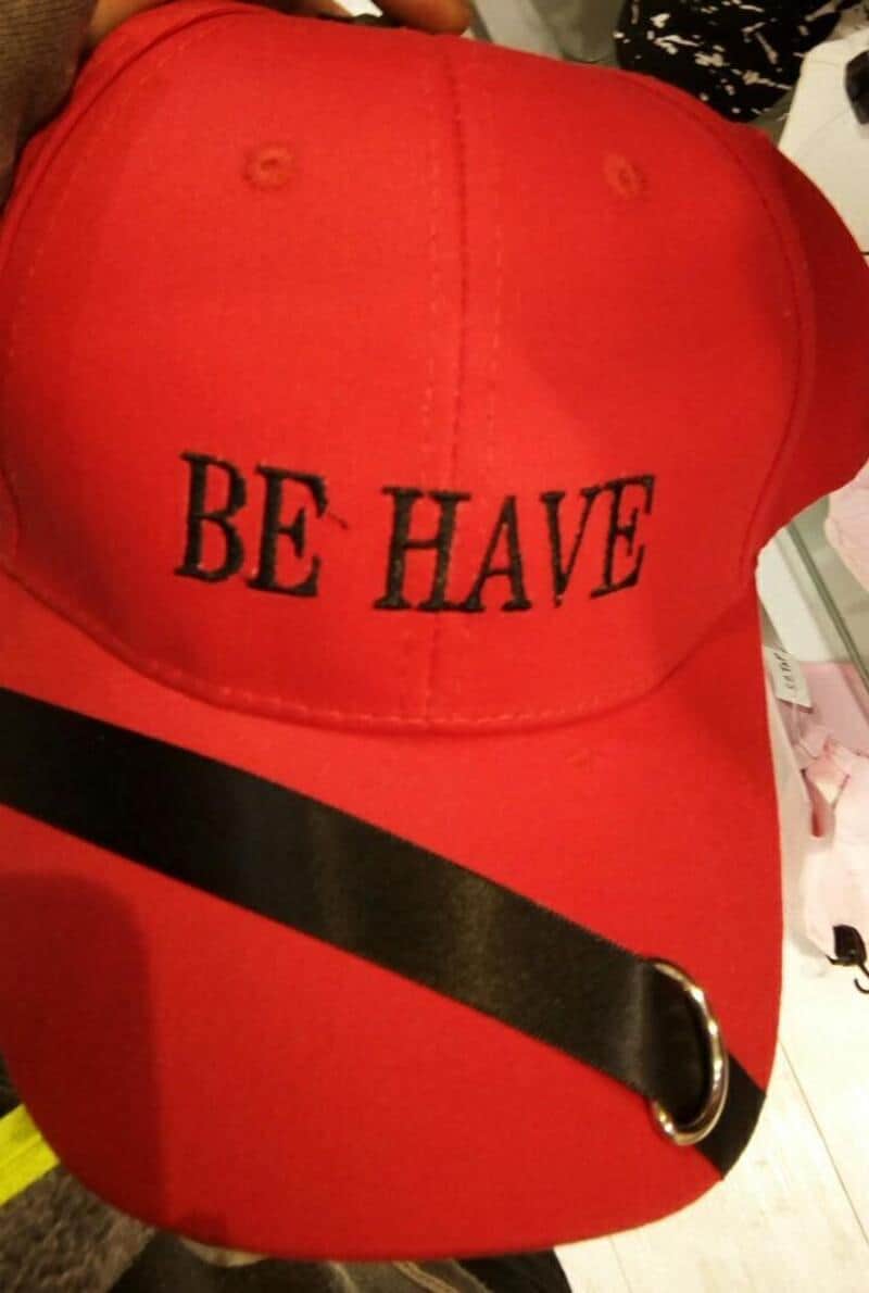Red cap with black embroidered text 'BE HAVE' and a black strap with a silver buckle.