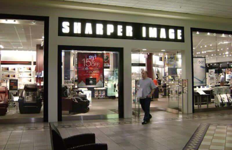 Shoppers enter a Sharpner Image store with bright signage and modern interior.