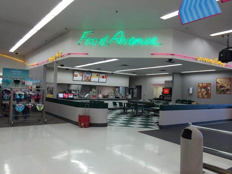 Food Avenue neon sign over a retro-style cafeteria counter inside a mall; green and pink accents; bl.