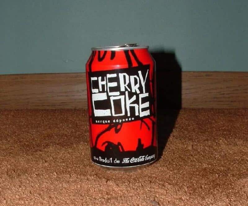 Cherry Coke can on a cork surface with teal wall in background.