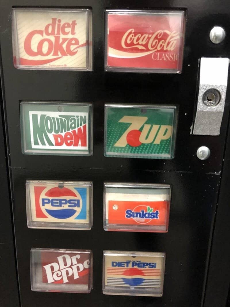 A vending machine displaying classic soda logos: Diet Coke, Coca-Cola Classic, Mountain Dew, 7up, Pe.