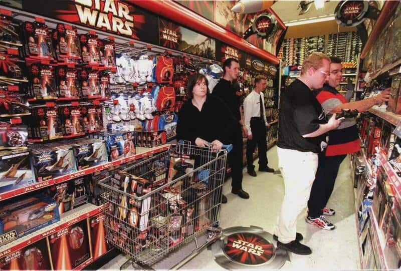 Shoppers in a Star Wars toy aisle with shelves of action figures and a shopping cart.