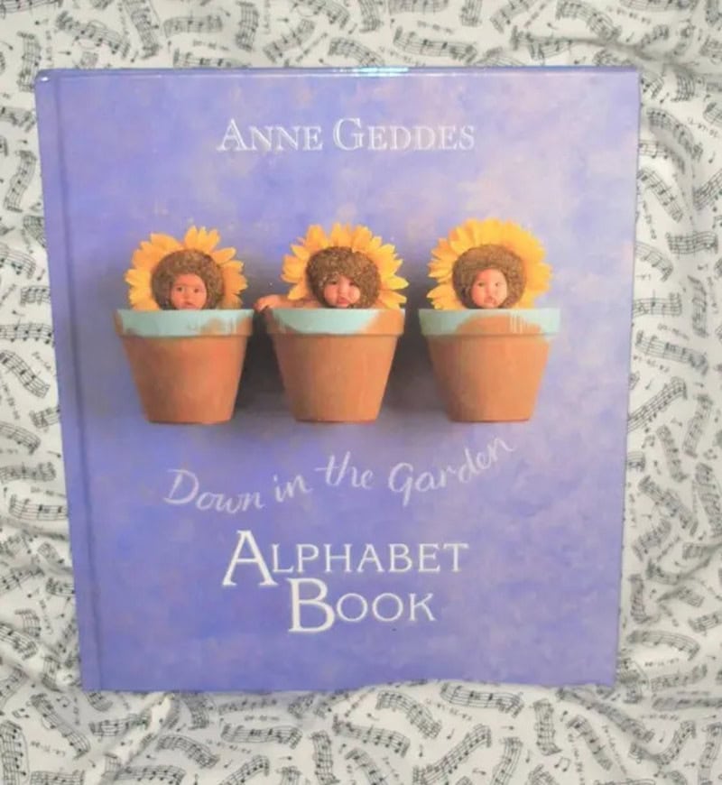 Three sunflowers in pots on a purple book cover, titled Down in the Garden Alphabet Book by Anne Ged.