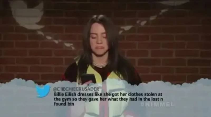 Girl with long dark hair and a yellow jacket, looking down, brick wall background.
