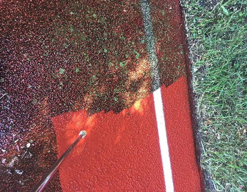 Power washing a red surface with a white line, showing before and after cleaning.