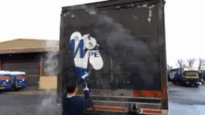Person power washing a large black truck with a logo on it.