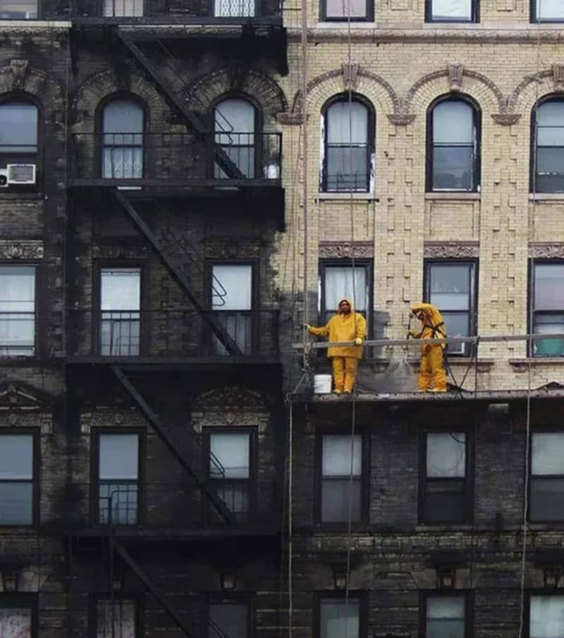 Two workers in yellow suits cleaning the building exterior.
