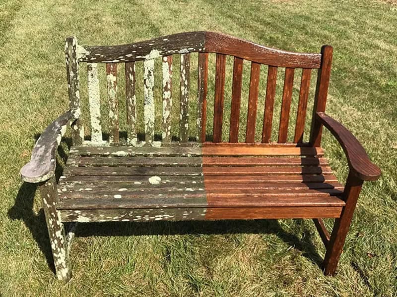 Before and after power washing of a wooden bench, showing weathered and cleaned sides.