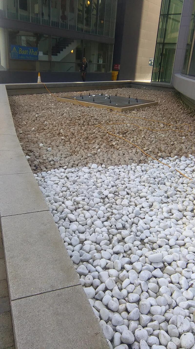 Before and after power washing of a pebble area outside a building.