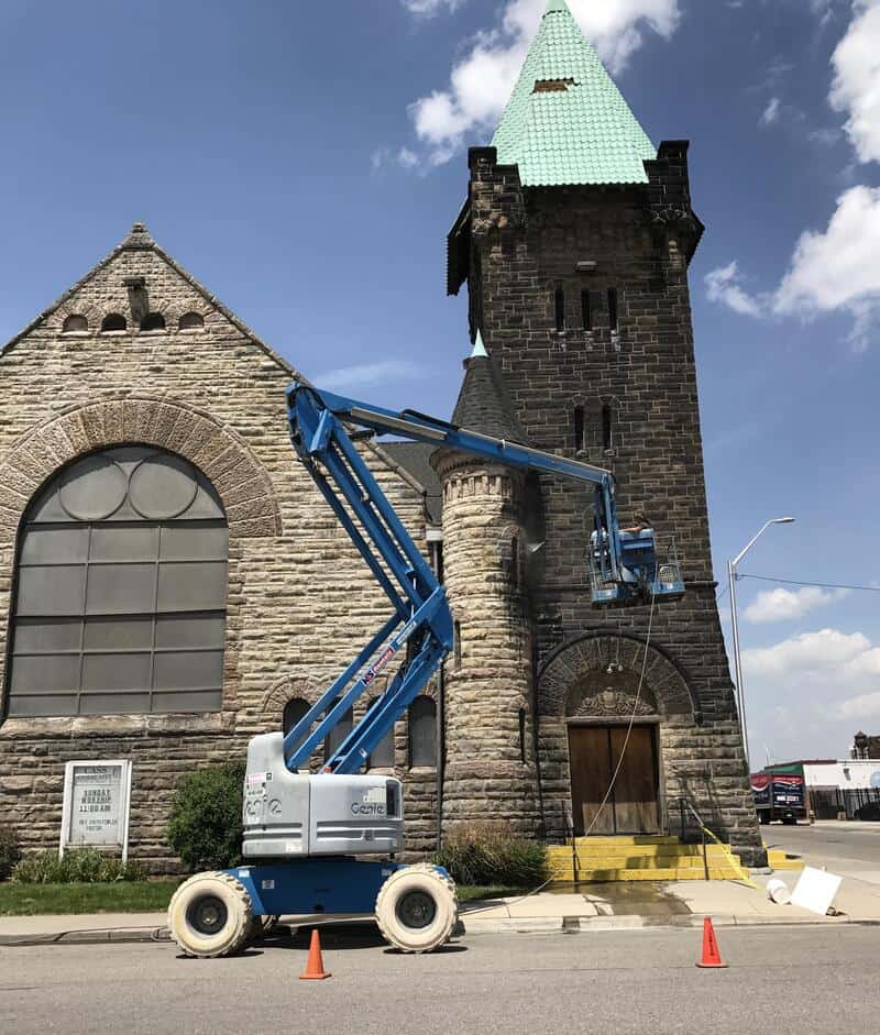 Power washing a historic stone building with a blue lift, orange cones on the street.