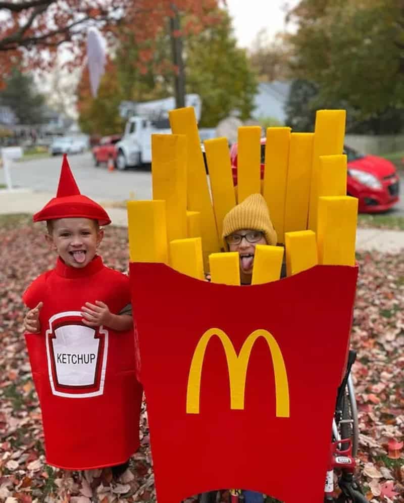 Two children in costume: one dressed as ketchup bottle and another as large McDonald's french fry.