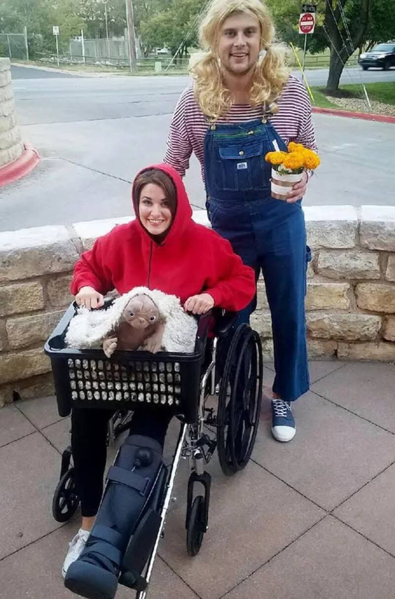 Two people outdoors: a person in a wheelchair with a red hoodie and a plush toy, and a person with a.