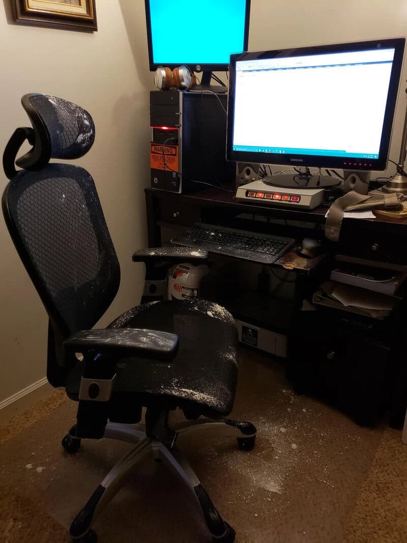 Office chair covered in dust in front of a computer desk with two monitors and a keyboard.