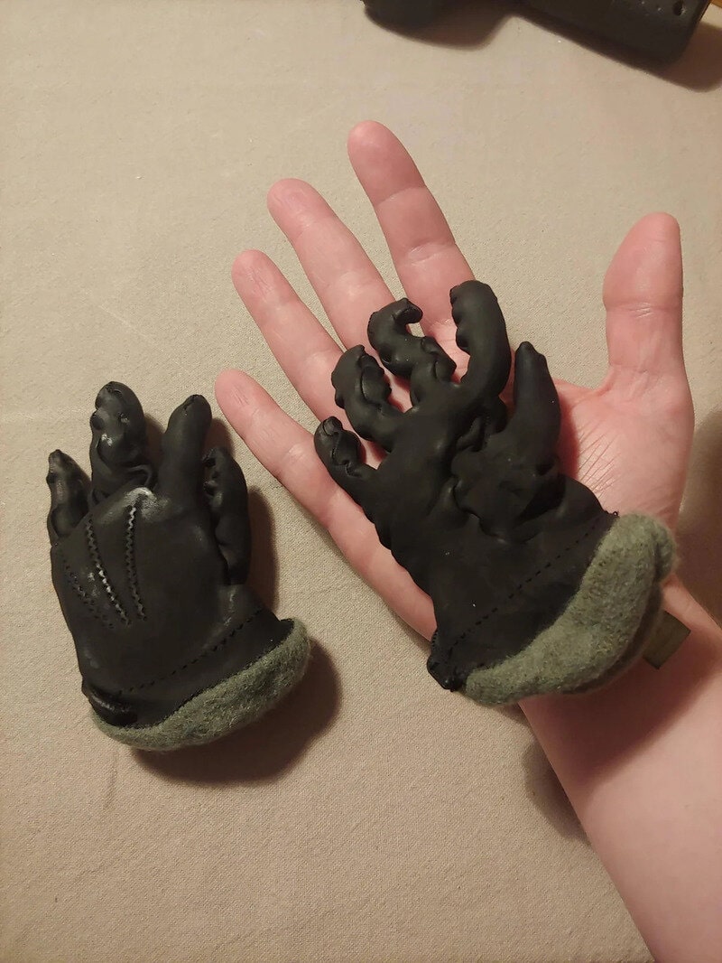 A person wearing black gloves with zombie-like fingers, holding a glove with a similar design.