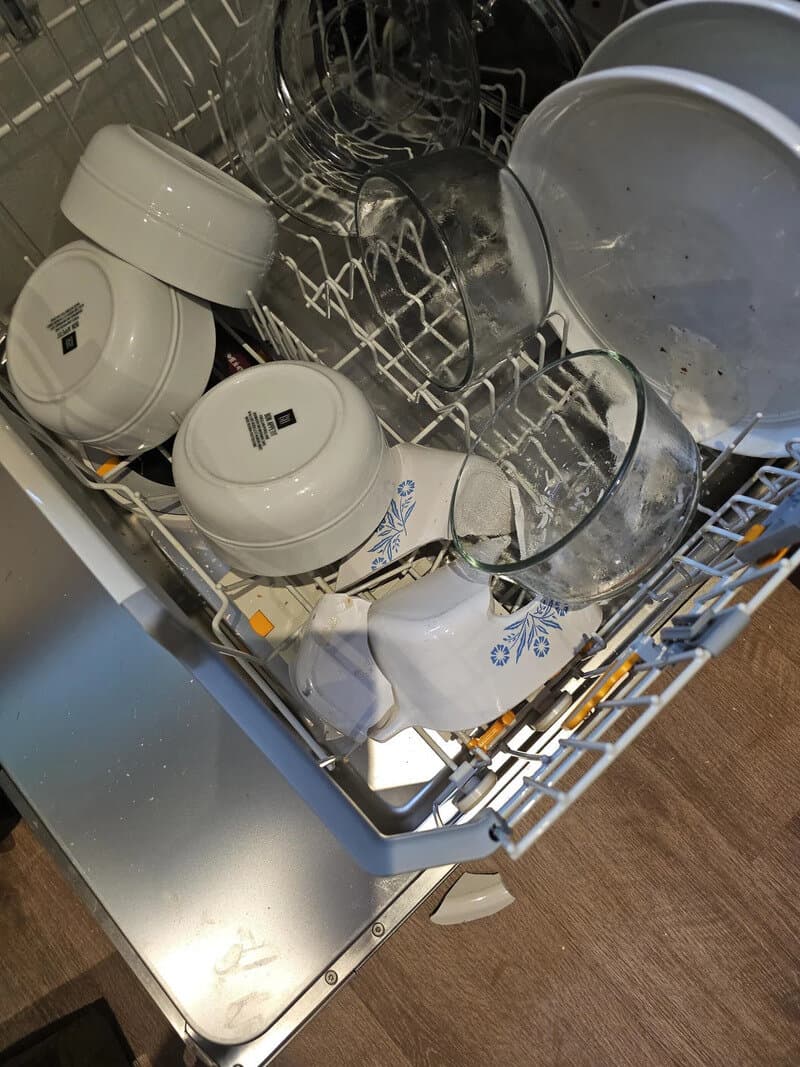 Dirty dishwasher with broken dishes and glasses inside.