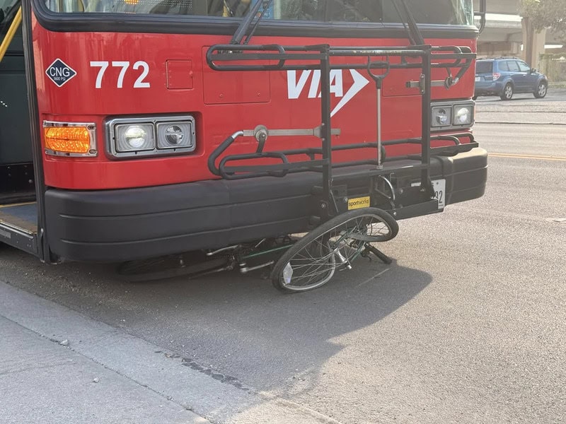 Red bus with bike rack and bicycle underneath, parked on street.