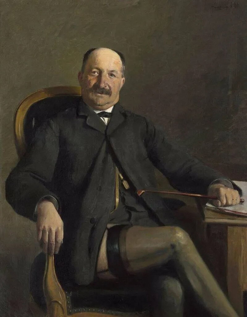Portrait of a man in a suit sitting in a chair with one leg crossed over the other.