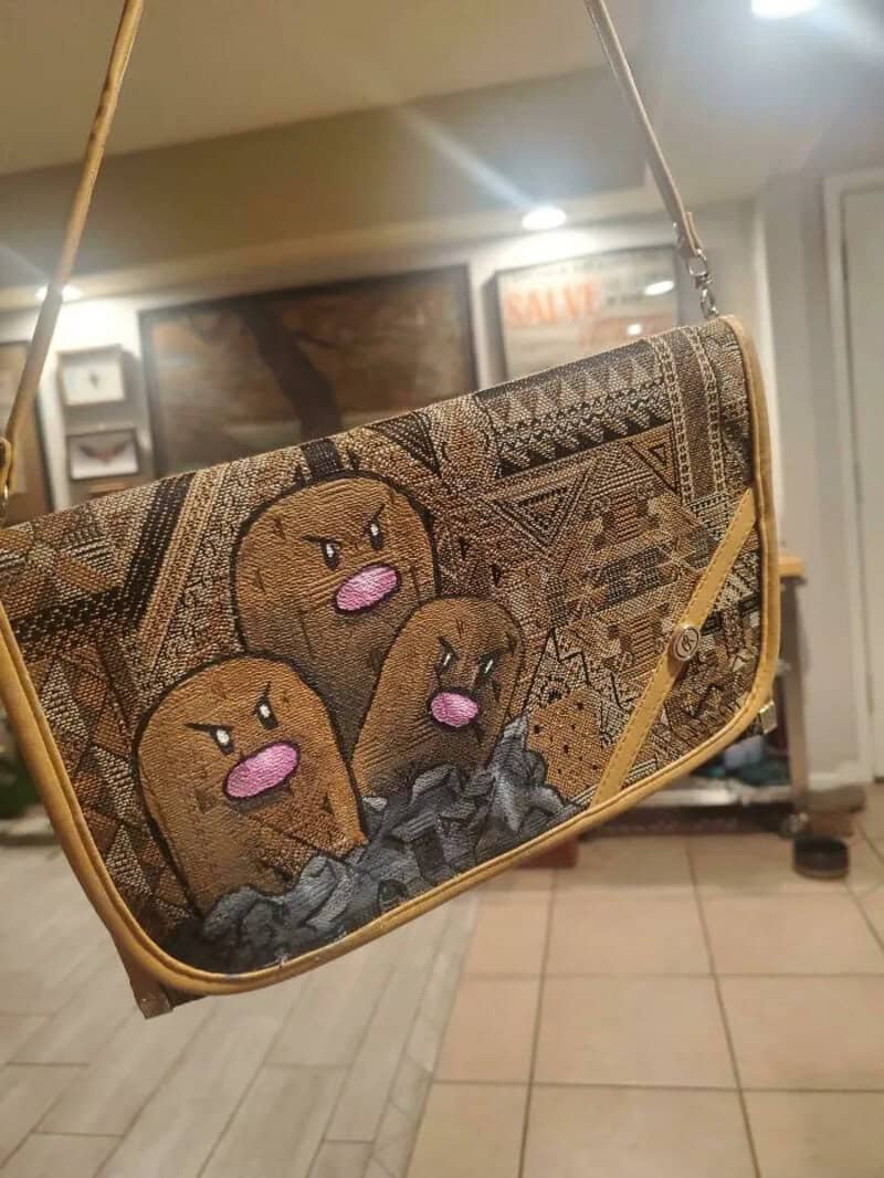 Handbag with cartoon faces and tribal patterns, hanging in a room.