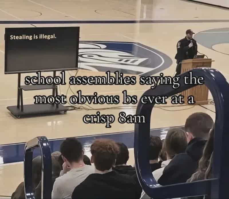 School assembly with a sign saying 'Stealing is illegal' and a speaker addressing students.