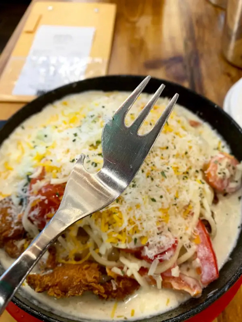 Fried chicken, cheese, and vegetables in a creamy sauce with a fork on top.