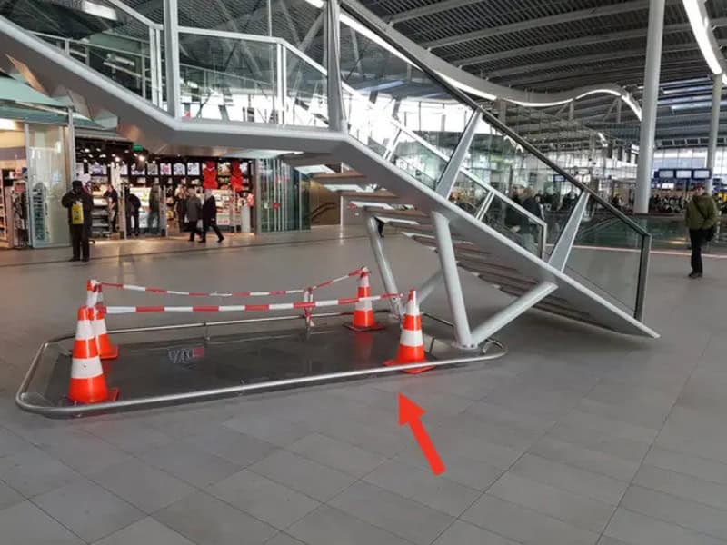 Escalator with a broken step and safety cones blocking it at an airport.