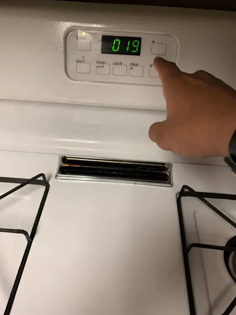 Person pressing a button on a stove with a digital display showing 019.
