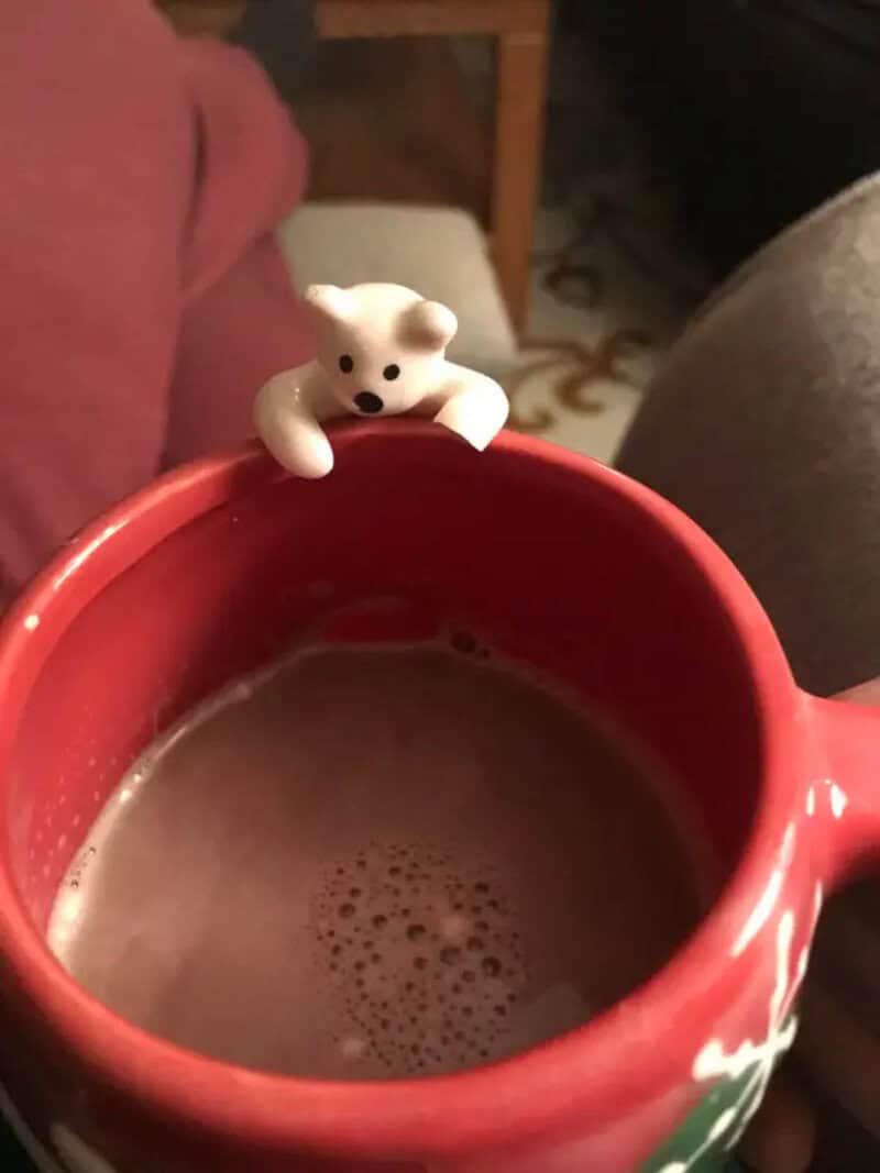 Small bear figurine on the edge of a red mug filled with a hot beverage.