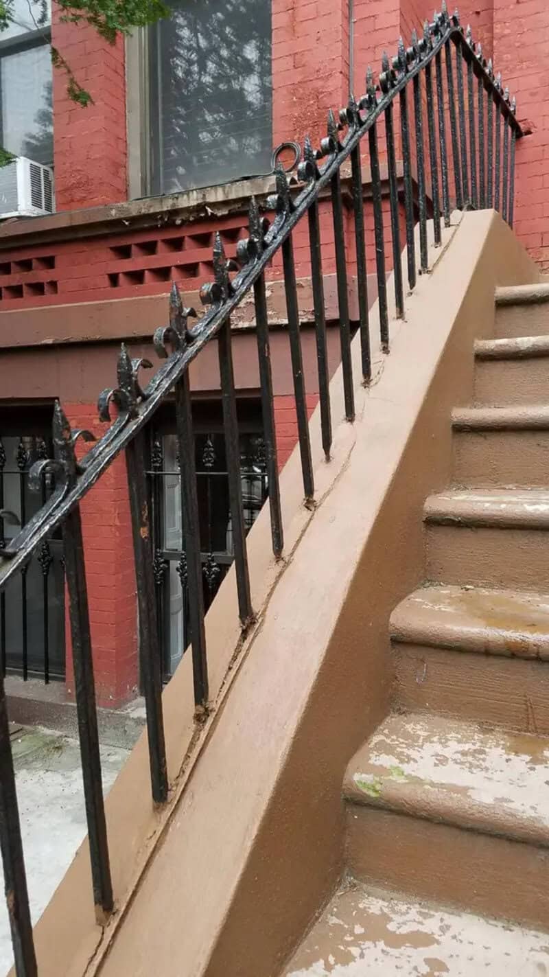 Steep outdoor stairs with a black metal railing and a brown concrete base.