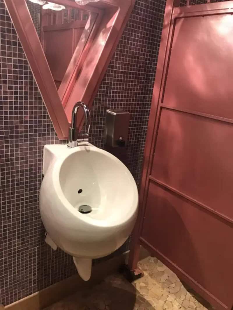 Urinal placed very close to a pink partition in a bathroom.
