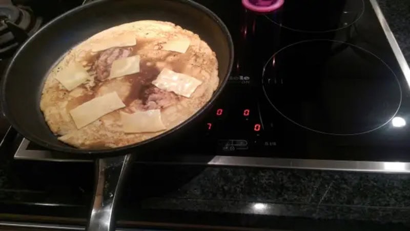 Frying pan with raw meat, cheese, and oil on an electric stove.