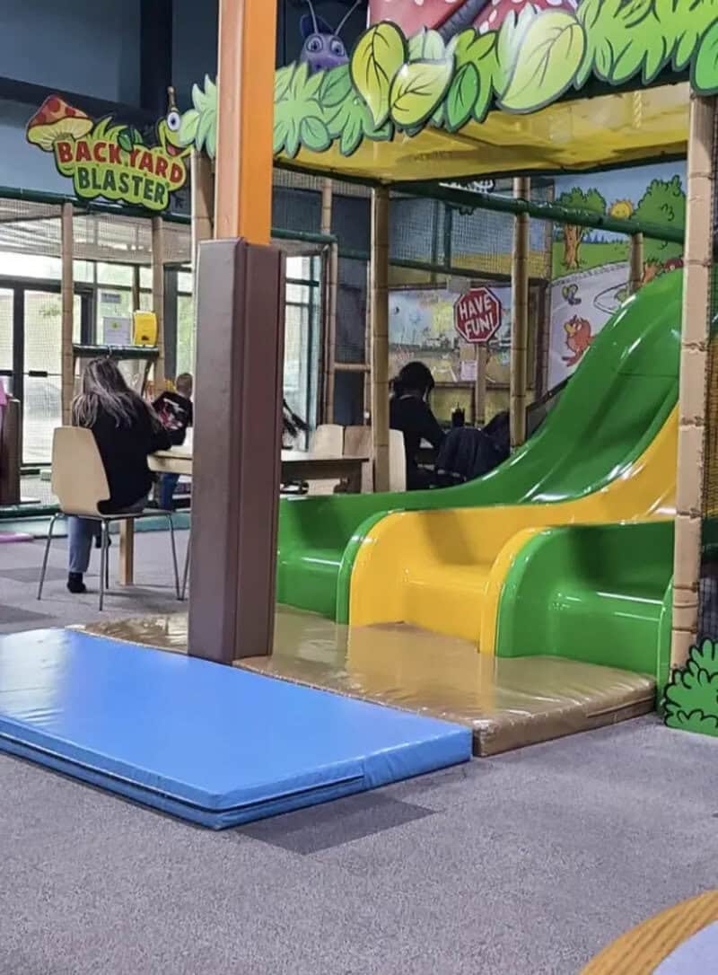 Colorful indoor playground with a slide and padded mat, part of a children's play area.