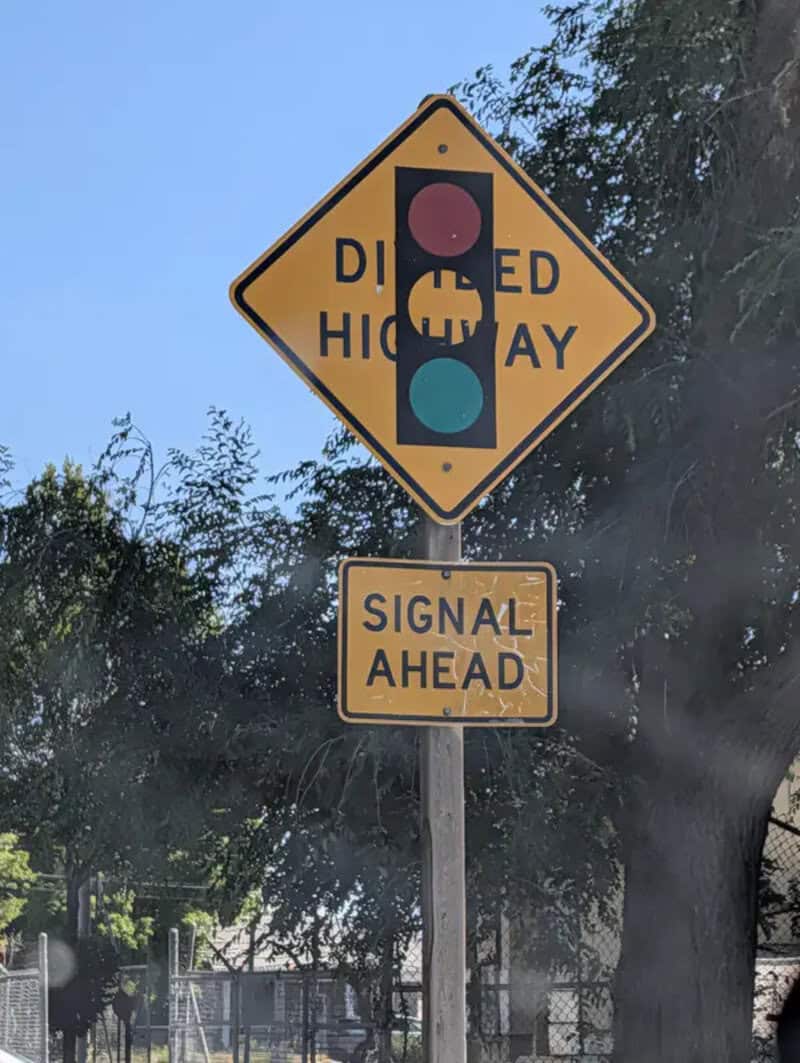 Dipped highway sign with traffic light and signal ahead warning.