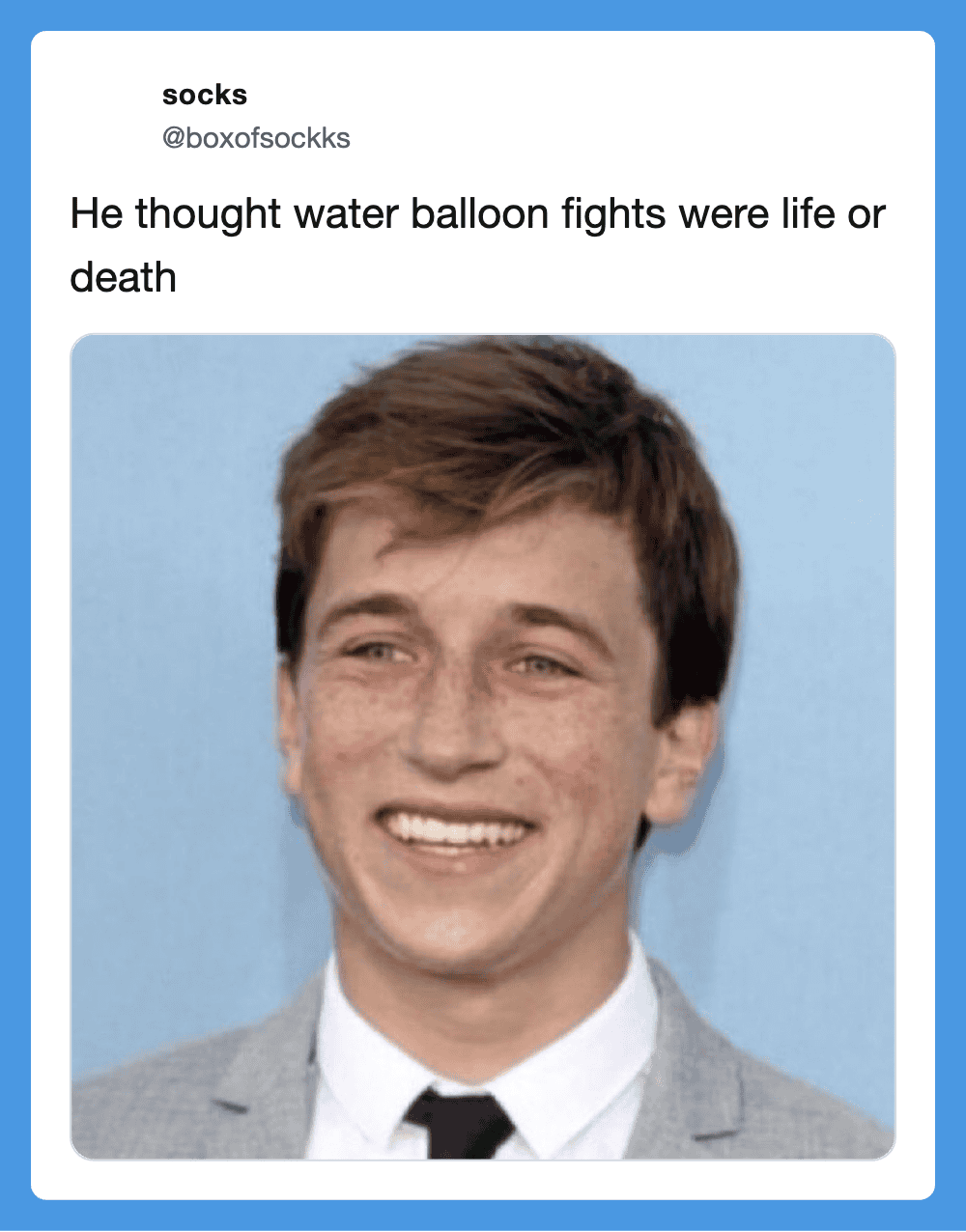Smiling young man in a suit with freckles, blue background.