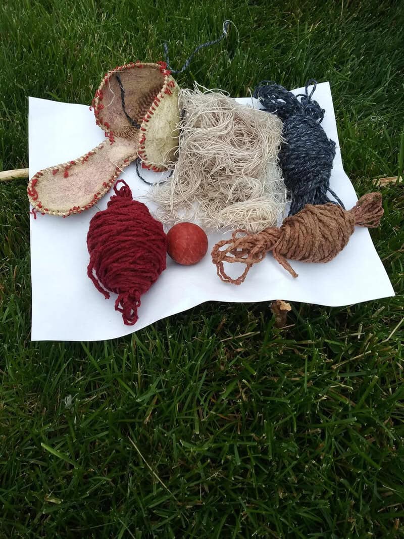 Assorted handmade yarn and fabric craft materials on white paper on grass.