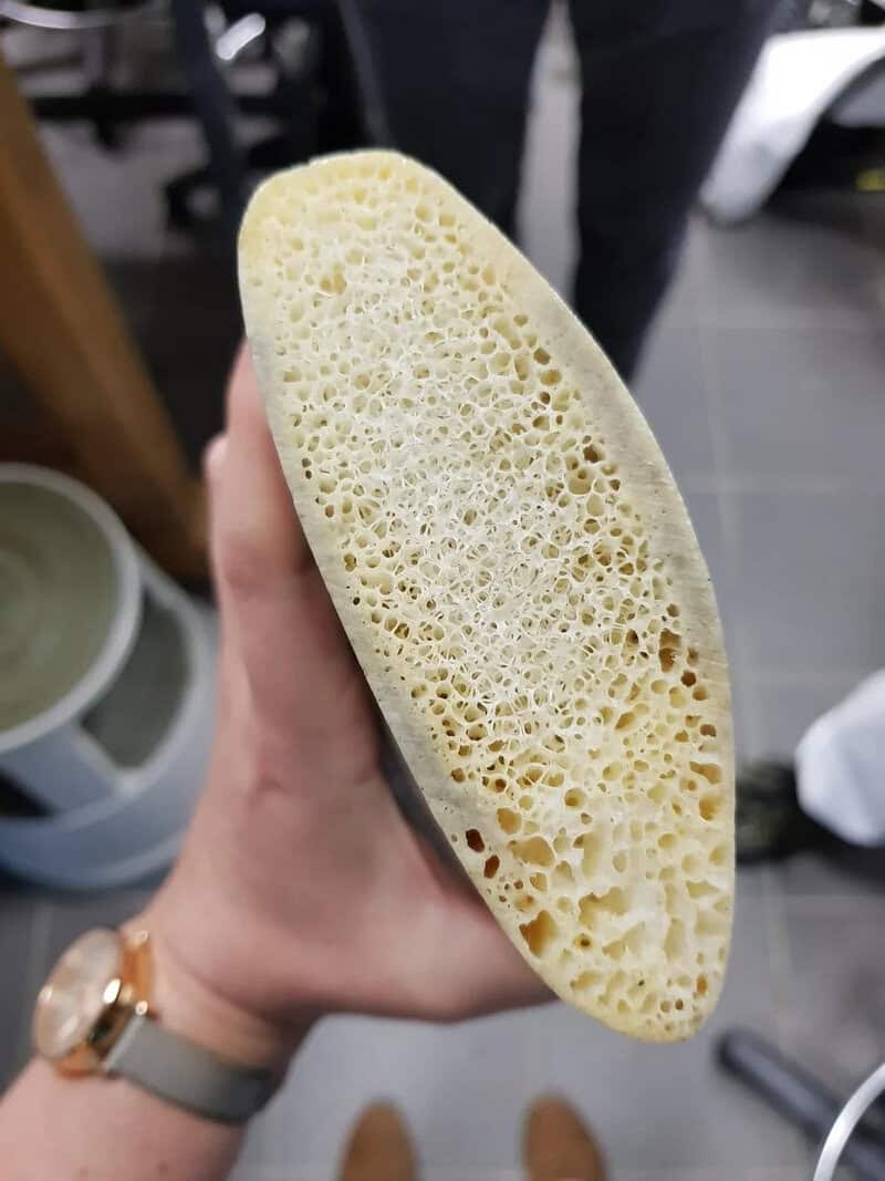 Close-up of a hand holding a yellow sponge with a porous surface.