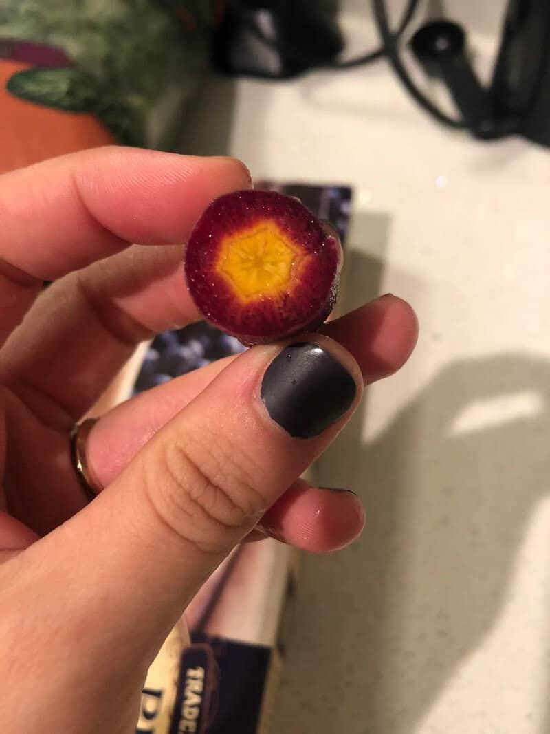 Close-up of a hand holding a halved cherry with a yellow star-shaped core.