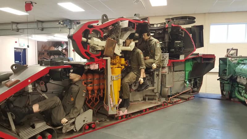 Soldiers inspecting a large military vehicle cut in half inside a workshop.