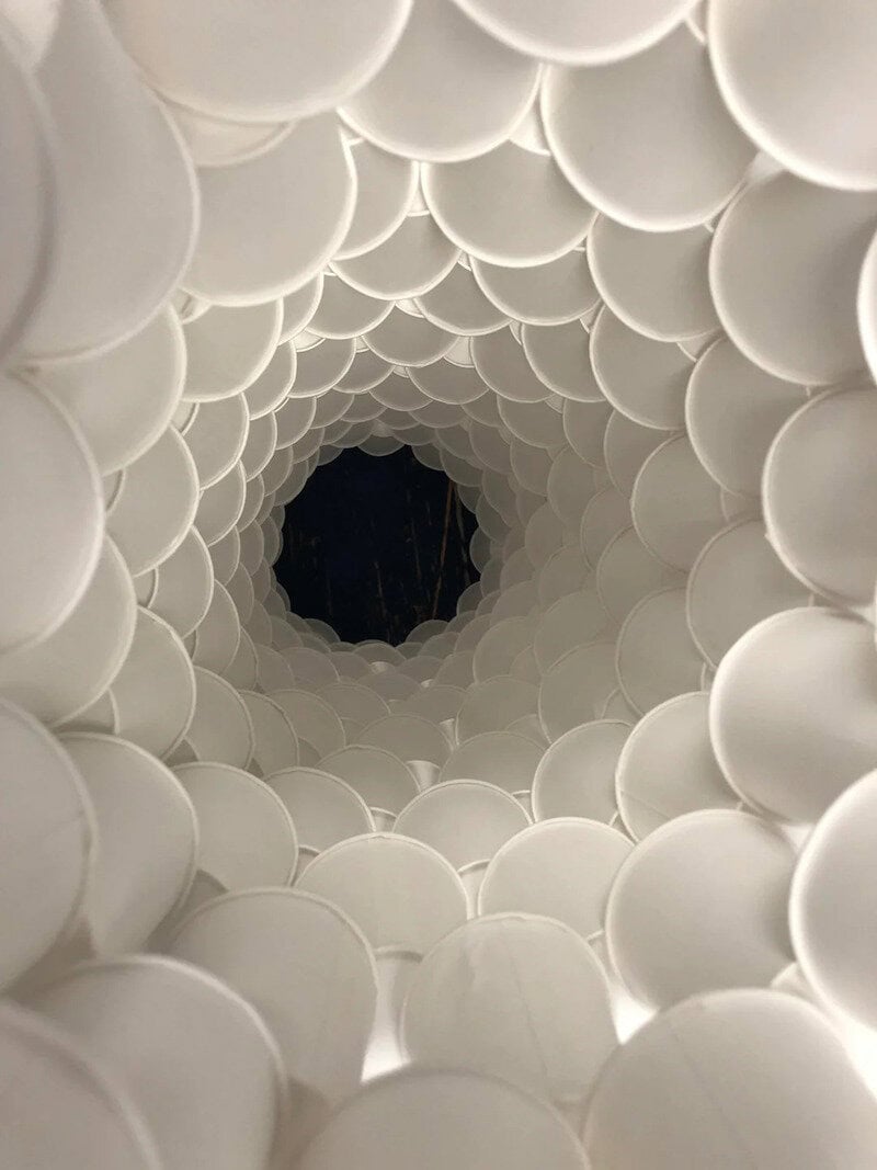 Looking down a tunnel made of white cups, creating a spiral pattern towards a dark center.
