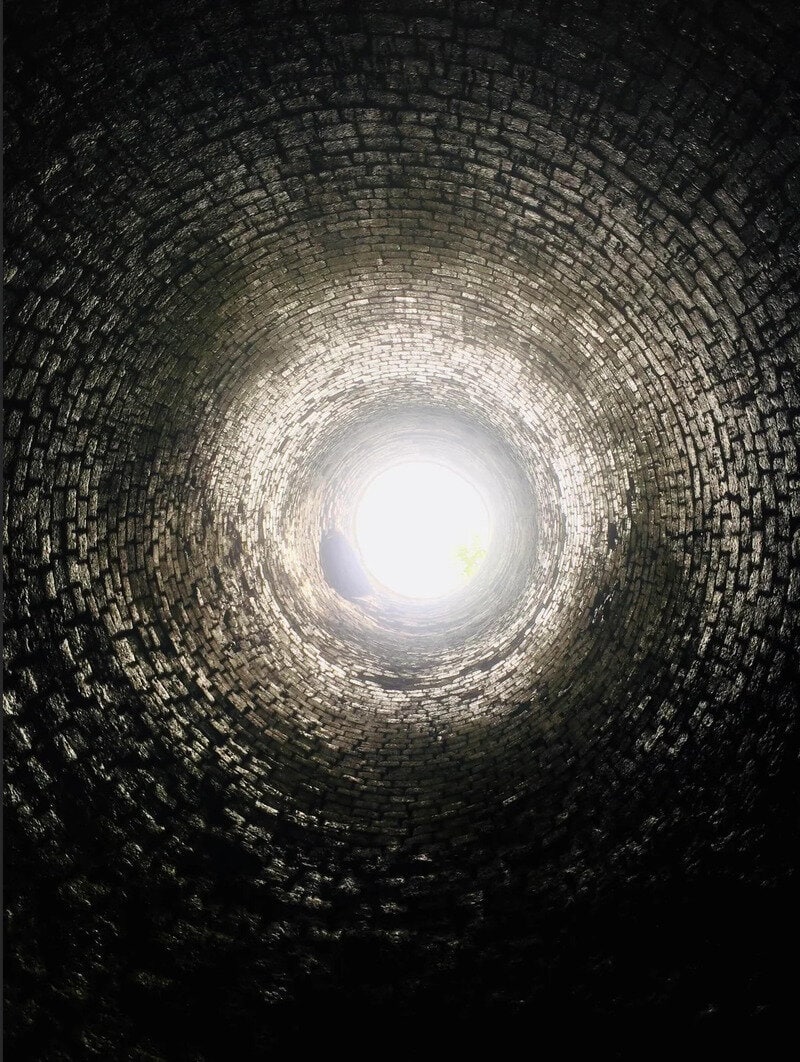 Looking up inside a dark brick well towards the bright opening at the top.