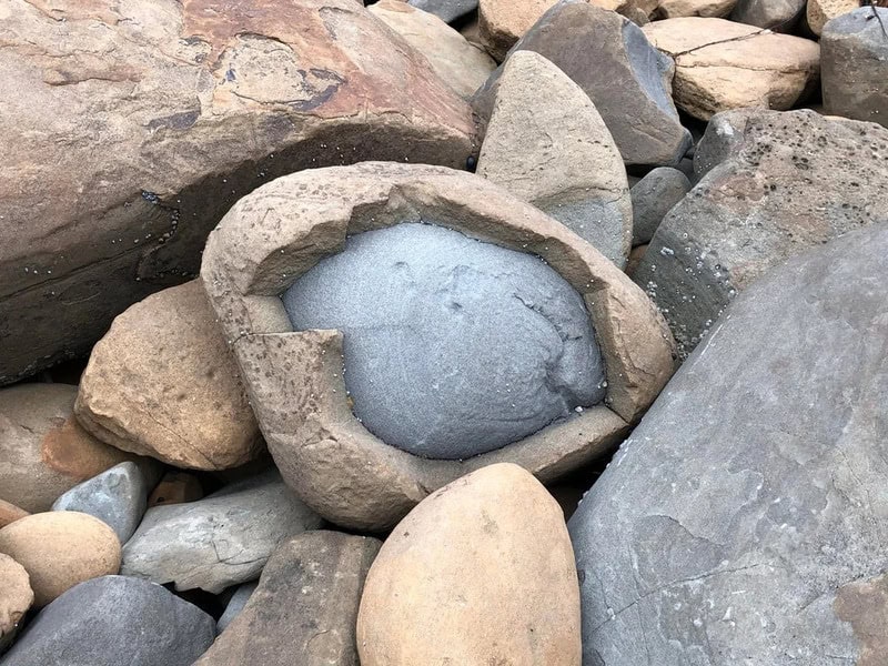 A rock with a hollowed-out center filled with cement among other stones.