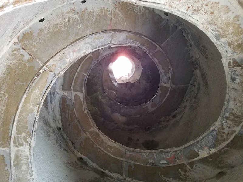 Looking up a stone spiral staircase with light at the top.