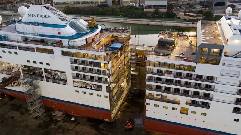 Two large cruise ships under construction at a shipyard, with scaffolding and construction equipment.
