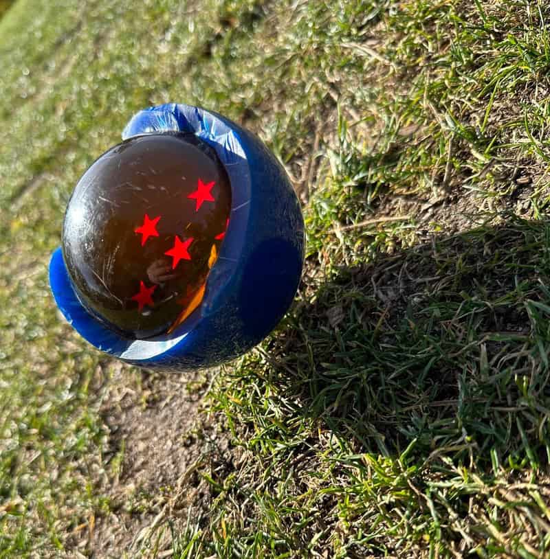 A black marble with red stars inside, resting on grass and dirt.