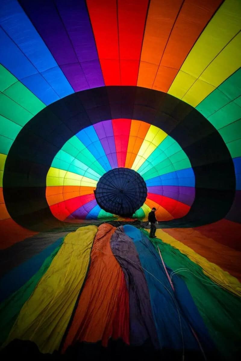 Colorful hot air balloon being inflated with a person nearby.