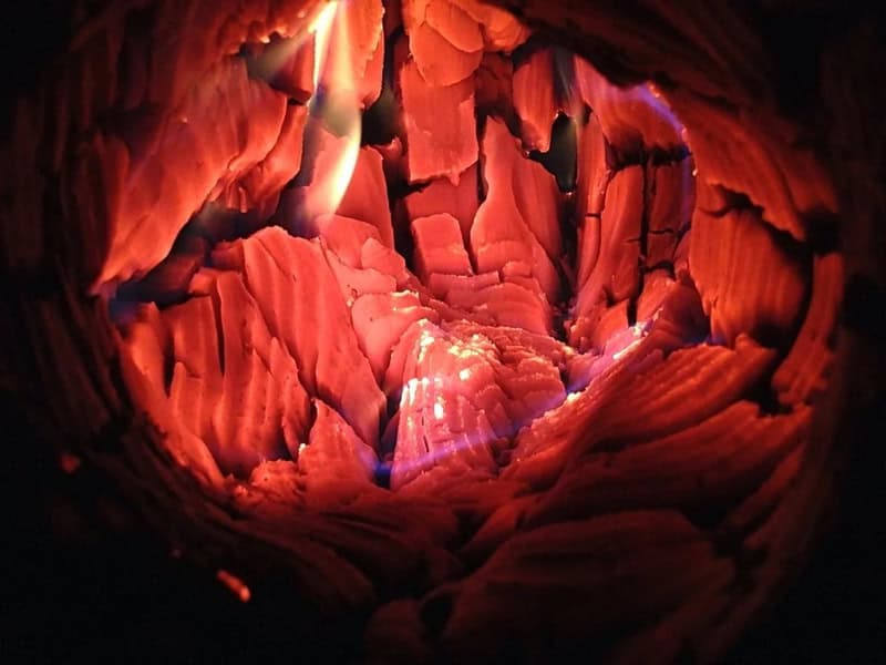 Close-up of a hollowed-out, glowing red and orange wooden log with cracks and textures.
