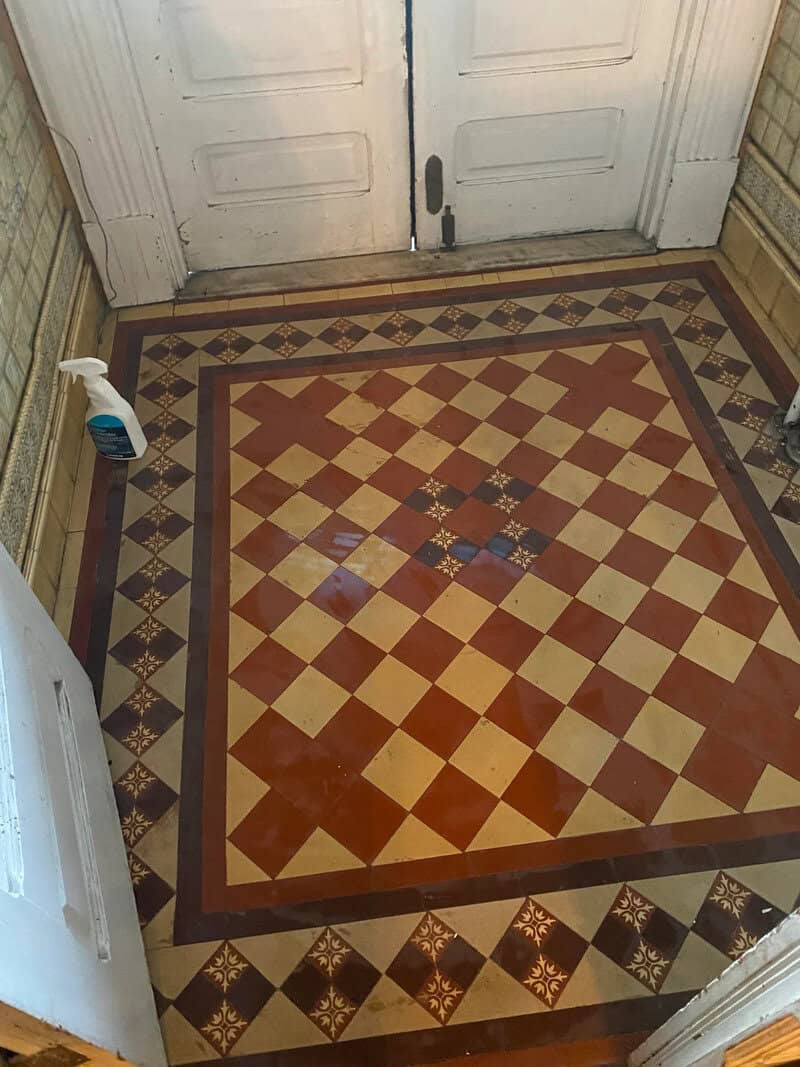 Vintage tiled floor with a door and cleaning spray in an old house.