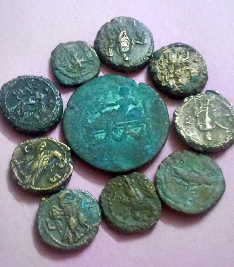 Ancient coins with various symbols and figures, some worn, on a pink background.