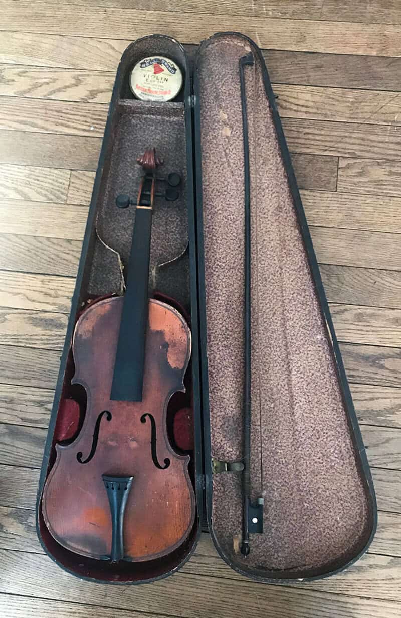 Old violin in a case with bow and rosin, on wooden floor.